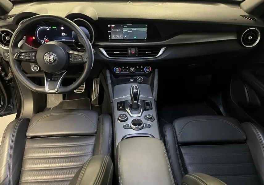 Vue intérieure frontale de l'Alfa Romeo Stelvio Veloce 2024, avec sièges sport cuir noir et console centrale moderne.