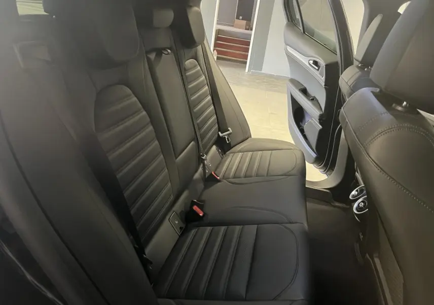 Vue intérieure arrière côté droit de l'Alfa Romeo Stelvio 2024 avec sièges sport en cuir noir et porte ouverte.