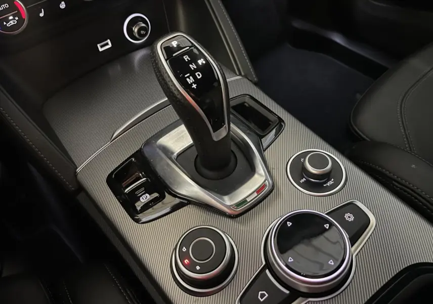 Gros plan sur la console centrale de l'Alfa Romeo Stelvio 2024, avec levier de vitesses automatique et commandes circulaires.