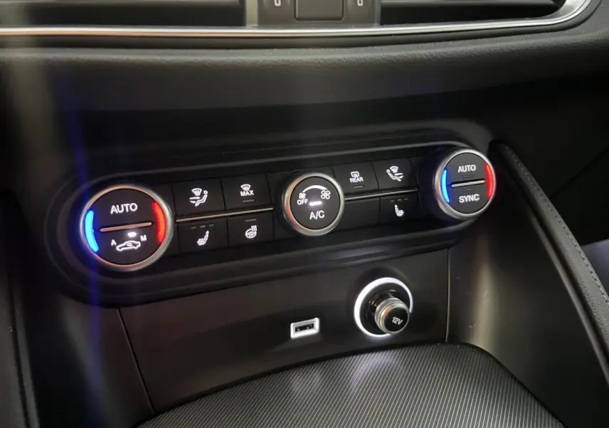 Gros plan sur la console centrale de l'Alfa Romeo Stelvio 2024, boutons de climatisation avec éclairage bleu et rouge.
