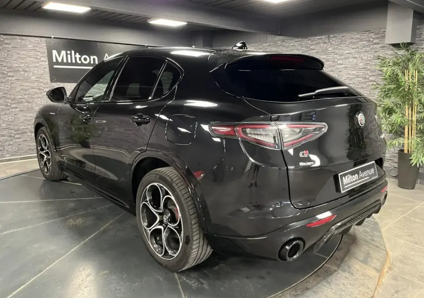 Vue 3/4 arrière droite d'un Alfa Romeo Stelvio Veloce noir Vulcano avec jantes 20 pouces et double sortie d'échappement noire.