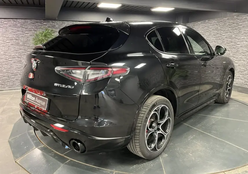 Vue 3/4 arrière droite de l'Alfa Romeo Stelvio Veloce noire avec jantes alliage 20 pouces et vitres surteintées.