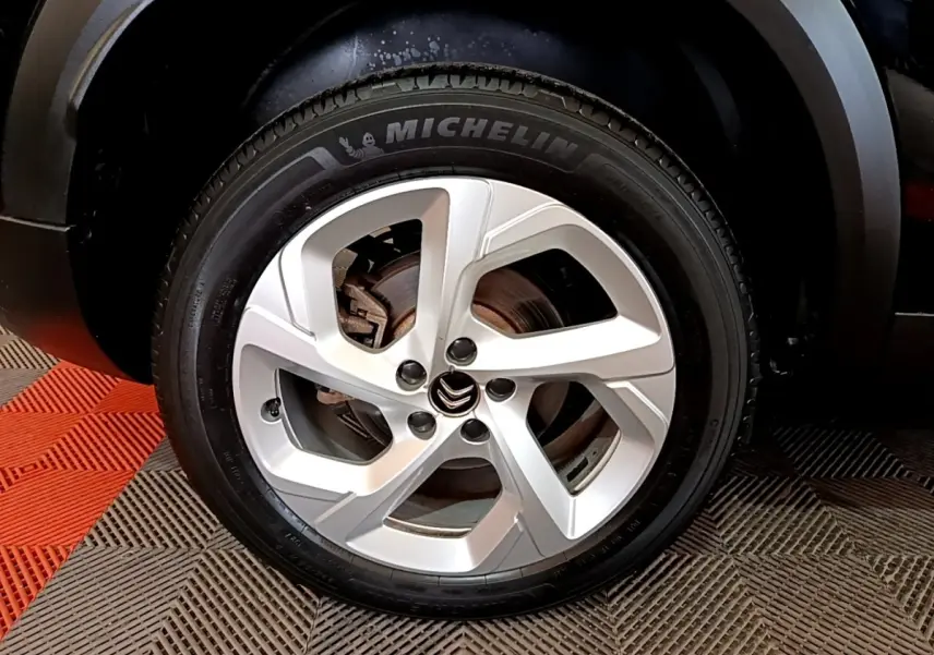 Gros plan sur la roue arrière droite noire d’un Citroën C5 Aircross hybride rechargeable 2022 sur sol carrelé rouge et gris.