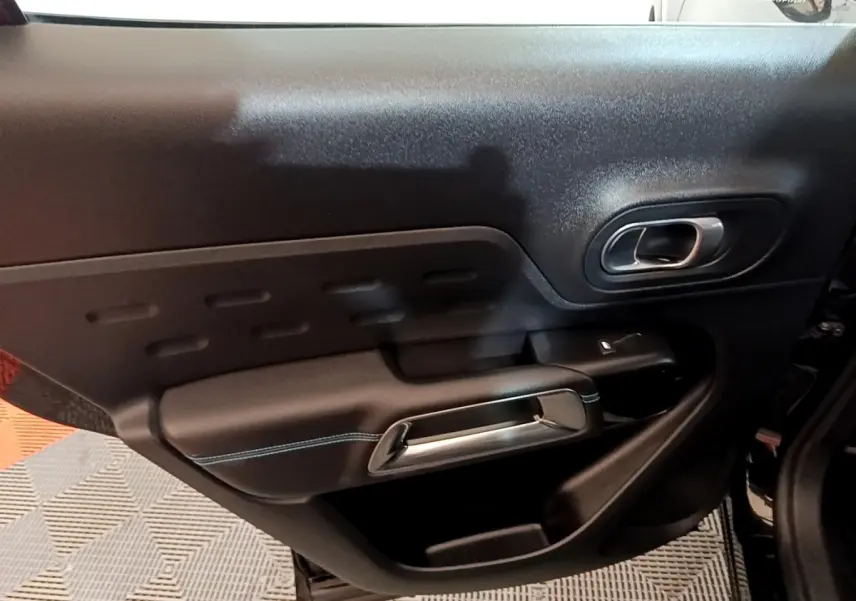 Gros plan sur la porte intérieure côté droit du Citroën C5 Aircross hybride noire, avec poignée argentée et surpiqûres bleues.