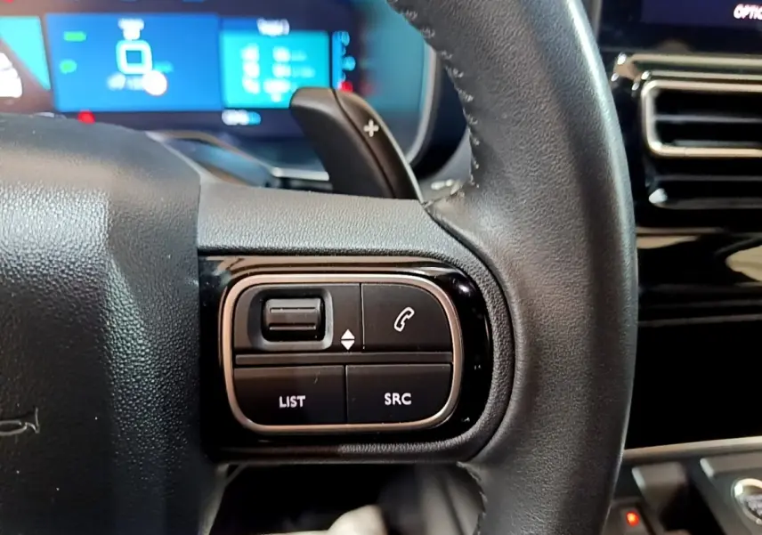 Gros plan sur les commandes gauche du volant cuir noir du Citroën C5 Aircross hybride rechargeable 2022, avec écran tactile en arrière-plan.