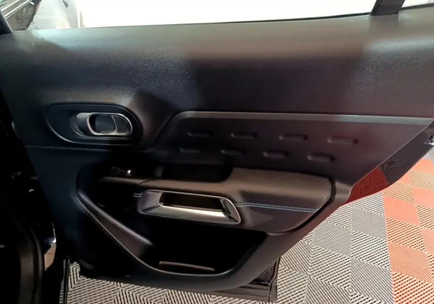 Vue intérieure de la porte arrière gauche noire du Citroën C5 Aircross hybride rechargeable avec poignée argentée et surpiqûres bleues.