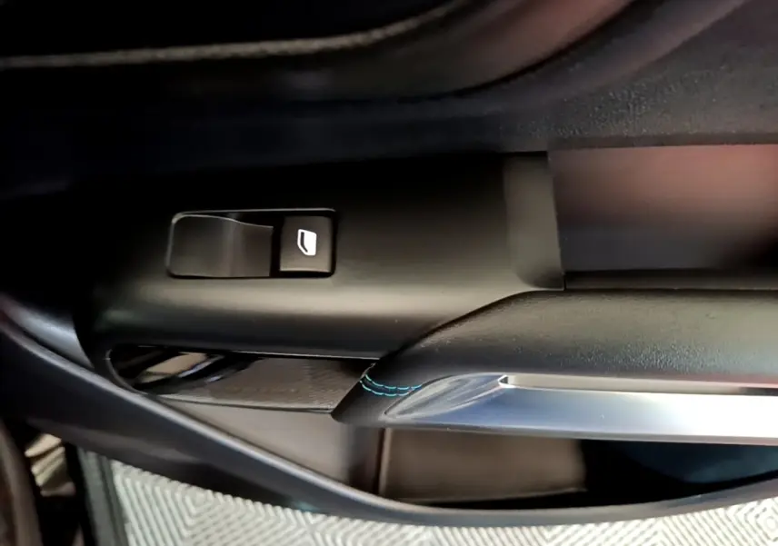 Détail de la commande de lève-vitre côté conducteur avec surpiqûres bleues sur garniture noire du Citroën C5 Aircross hybride.