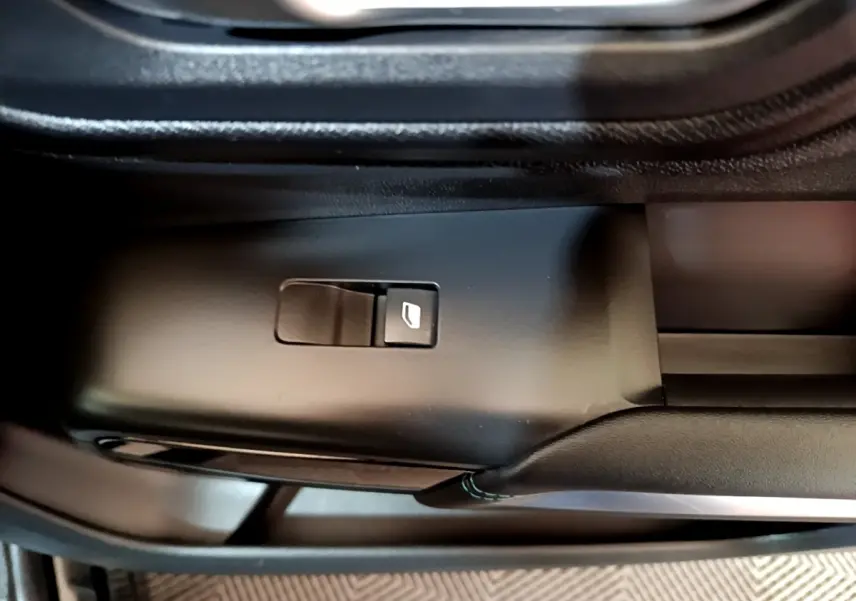 Gros plan sur le bouton de commande de la vitre électrique côté conducteur dans l'habitacle noir du Citroën C5 Aircross hybride.