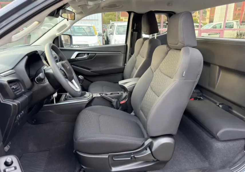 Vue intérieure côté conducteur du pick-up Isuzu D-MAX 2.2 TD 164 Space Evolution, sièges tissu gris et accoudoir central.