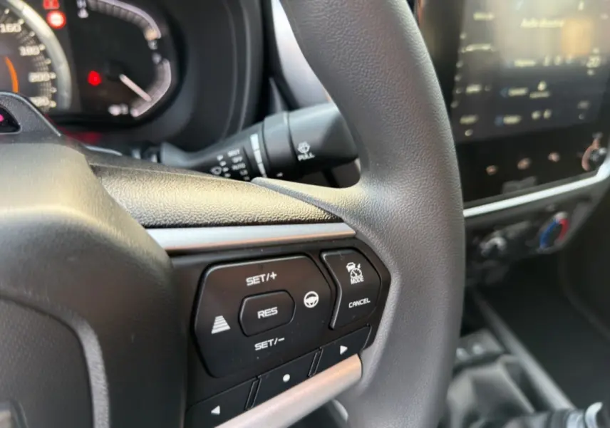 Gros plan sur le volant multifonctions noir de l'Isuzu D-MAX 2026 avec commandes de régulateur et écran tactile flou en arrière-plan.