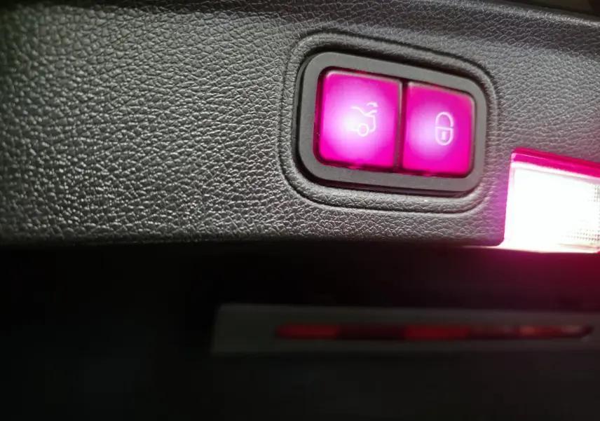 Gros plan sur les boutons lumineux de déverrouillage du coffre et de verrouillage central dans le coffre d'une Mercedes Classe C Coupé gris.