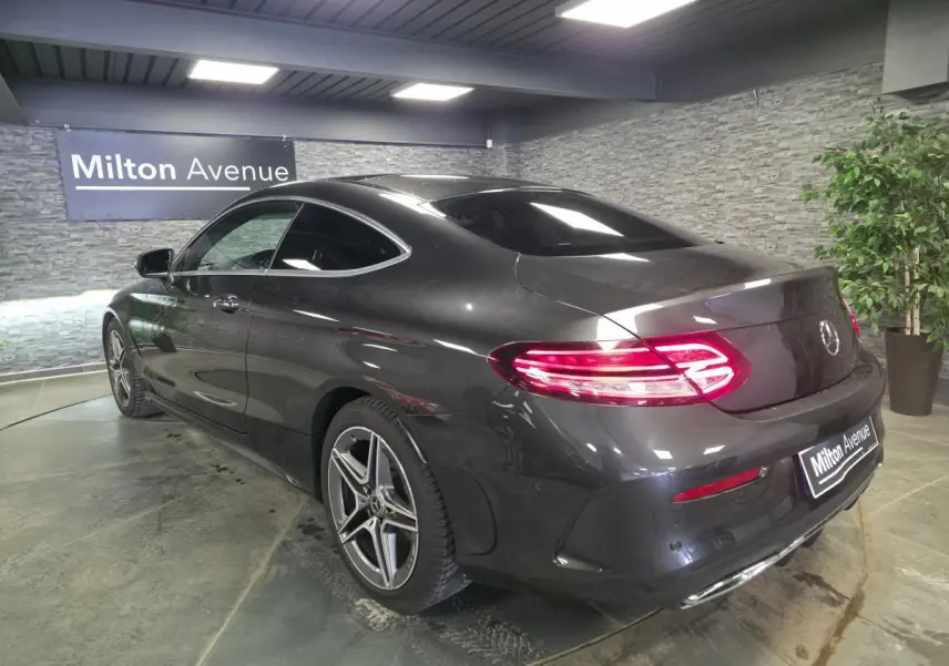 Vue 3/4 arrière droite d'une Mercedes Classe C Coupé gris métallisé avec jantes AMG 18 pouces et feux LED allumés.