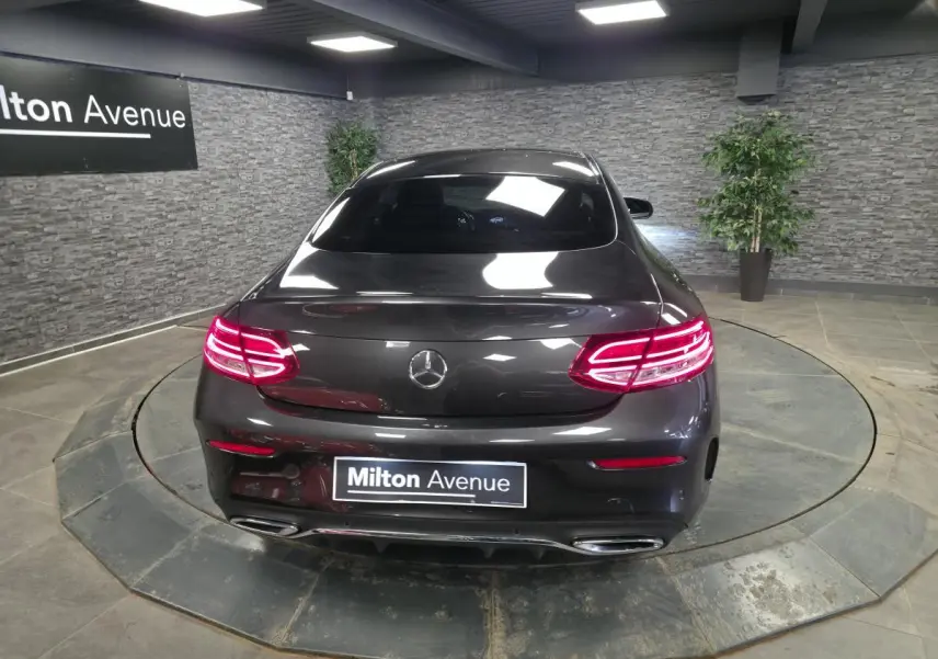 Vue arrière d'une Mercedes Classe C Coupé gris métallisé avec feux LED allumés dans un showroom.