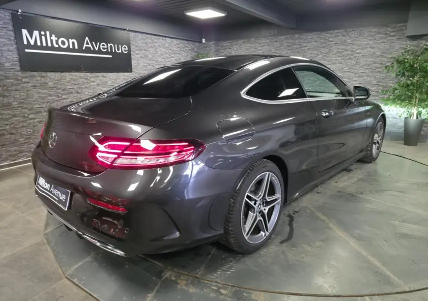 Vue 3/4 arrière droit d'une Mercedes Classe C Coupé gris métallisé avec jantes AMG 18 pouces et feux arrière LED allumés.