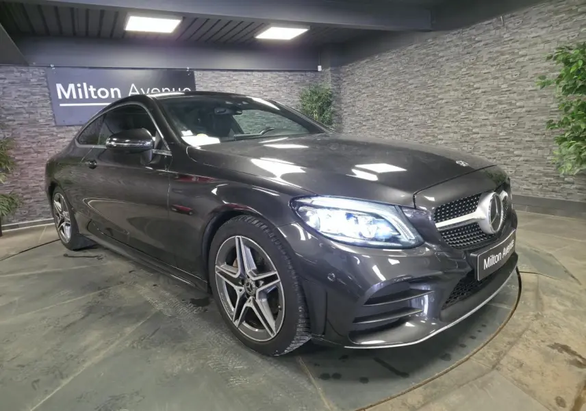 Mercedes Classe C Coupé gris métallisé en 3/4 avant droit avec jantes AMG 18 pouces et projecteurs LED allumés.