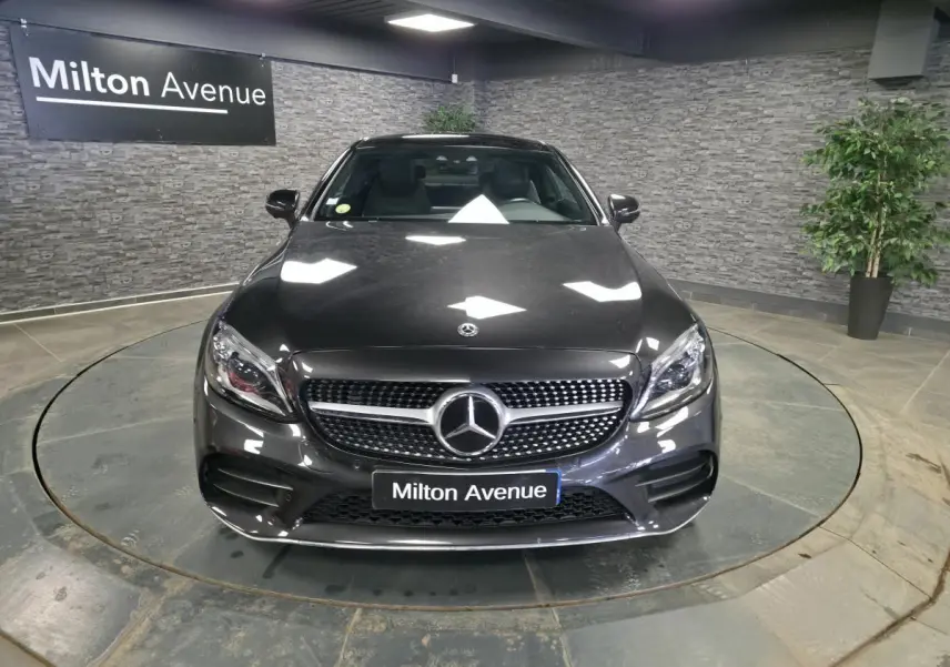 Mercedes Classe C Coupé gris métallisé vu de face dans un showroom avec calandre AMG et logo étoile bien visibles.