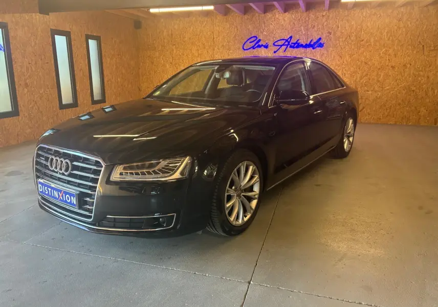 Audi A8 3.0 TDI noire vue en 3/4 avant droit dans un showroom avec éclairage chaud et murs en bois.
