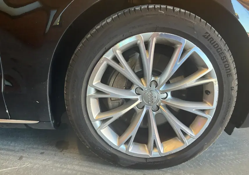 Gros plan sur la roue avant droite d'une Audi A8 noire 2016, avec jante alliage argentée à multiples branches fines.