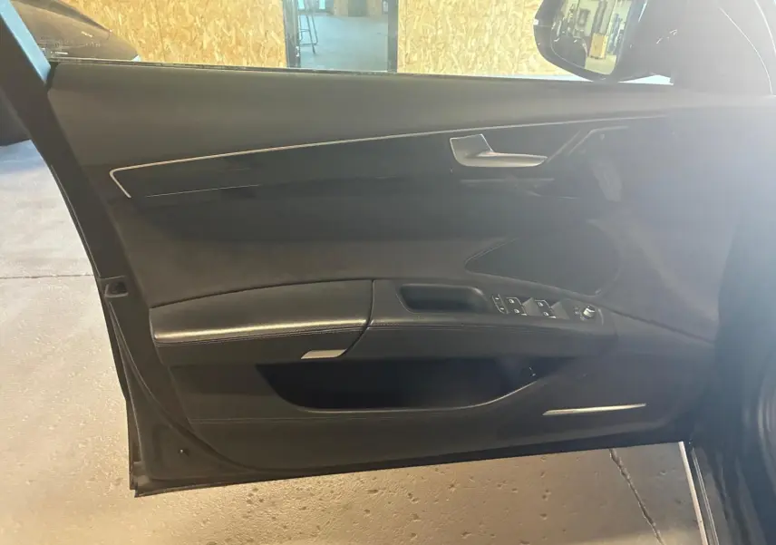 Vue intérieure de la porte avant gauche noire d'une Audi A8 2016, avec commandes de vitres et garniture cuir.