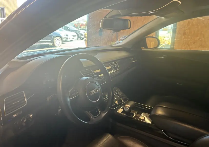 Vue intérieure côté conducteur de l'Audi A8 noire 2016, mettant en valeur le volant multifonction et la console centrale.