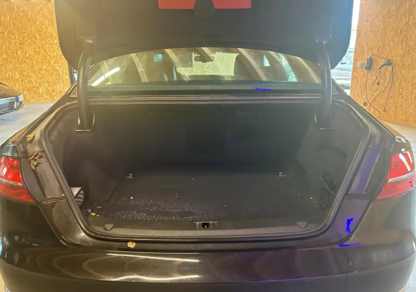Vue arrière d’un coffre ouvert d’Audi A8 noire 2016, montrant l’espace de rangement vide et les feux arrière allumés.