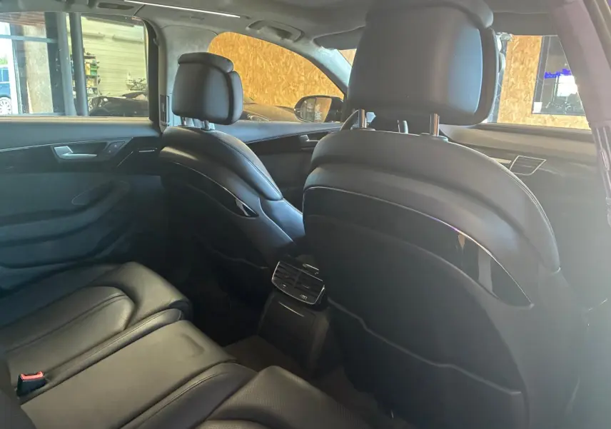 Vue intérieure arrière de l'Audi A8 2016 noire, montrant les sièges en cuir et la console centrale avec aérateurs.