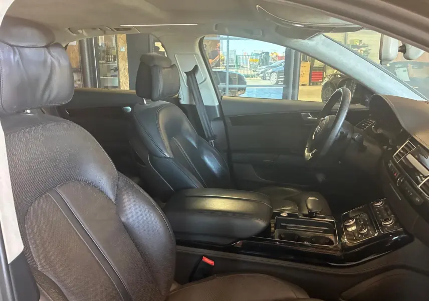 Vue intérieure côté conducteur de l'Audi A8 2016, sièges cuir noirs et console centrale avec commandes intégrées.