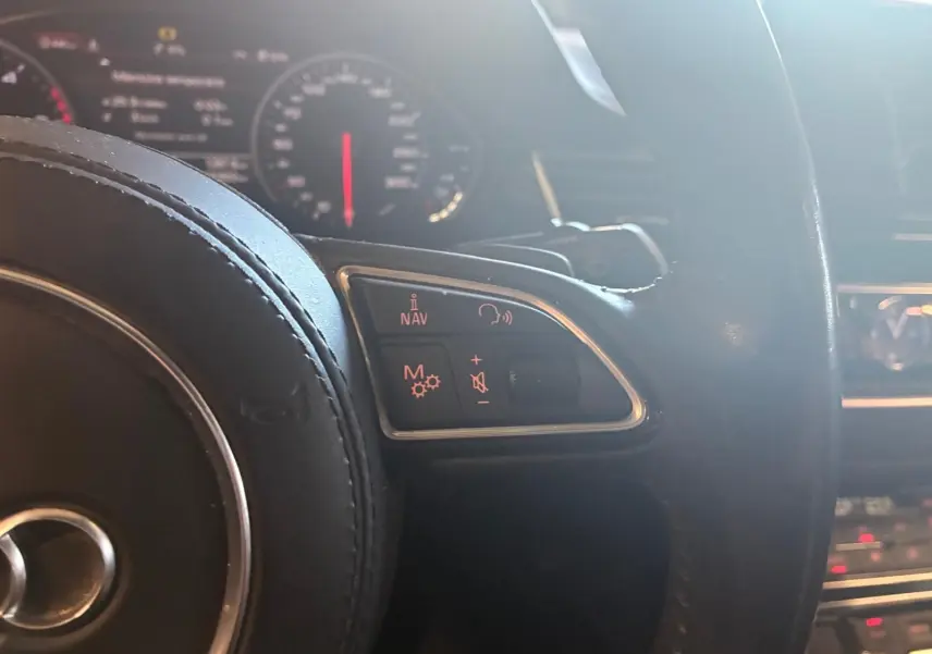 Vue rapprochée du volant noir de l'Audi A8 2016, avec commandes audio et navigation illuminées en rouge.