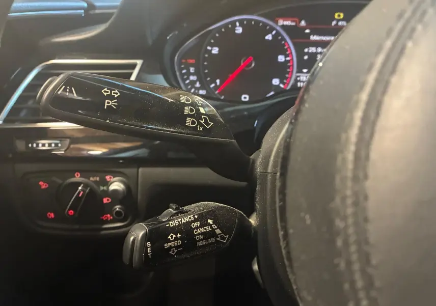 Gros plan sur les commandes au volant noir d'une Audi A8 2016, avec tableau de bord digital en arrière-plan.