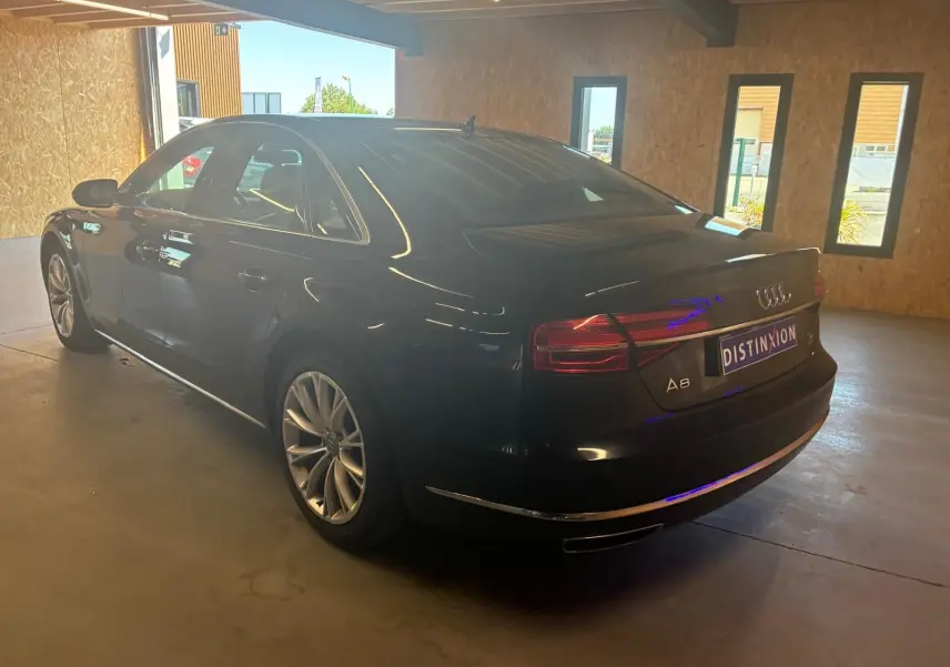 Audi A8 noir vue en 3/4 arrière droit dans un garage, avec feux arrière allumés et jantes alliage visibles.