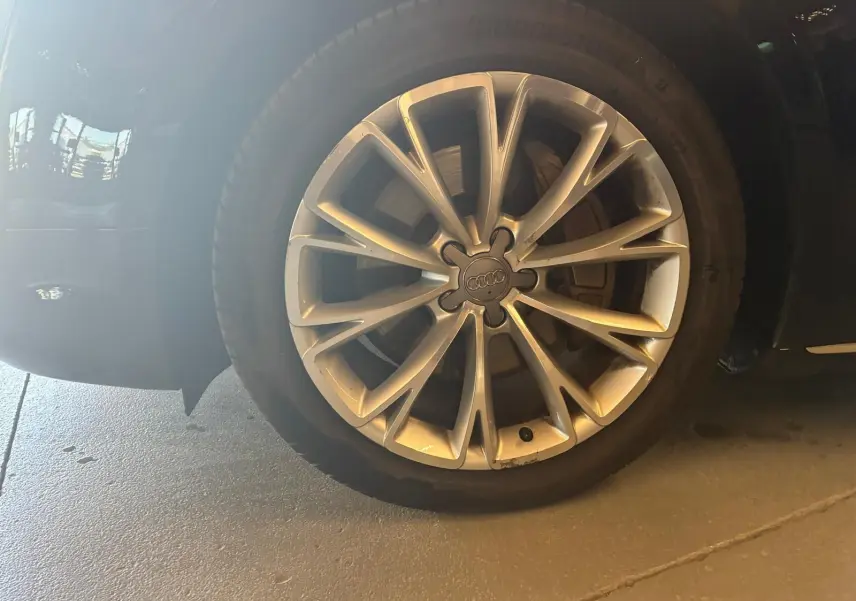 Gros plan sur la roue avant droite d’une Audi A8 noire 2016, mettant en valeur la jante en alliage au design complexe.