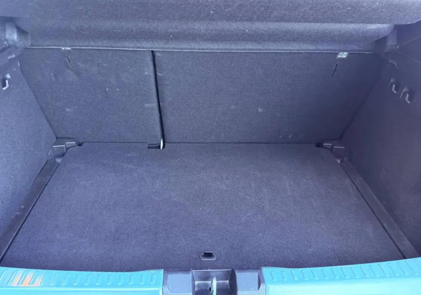 Coffre ouvert d'une Dacia Sandero 2025, vue intérieure, revêtement noir et seuil de coffre vert cèdre métallisé visible.