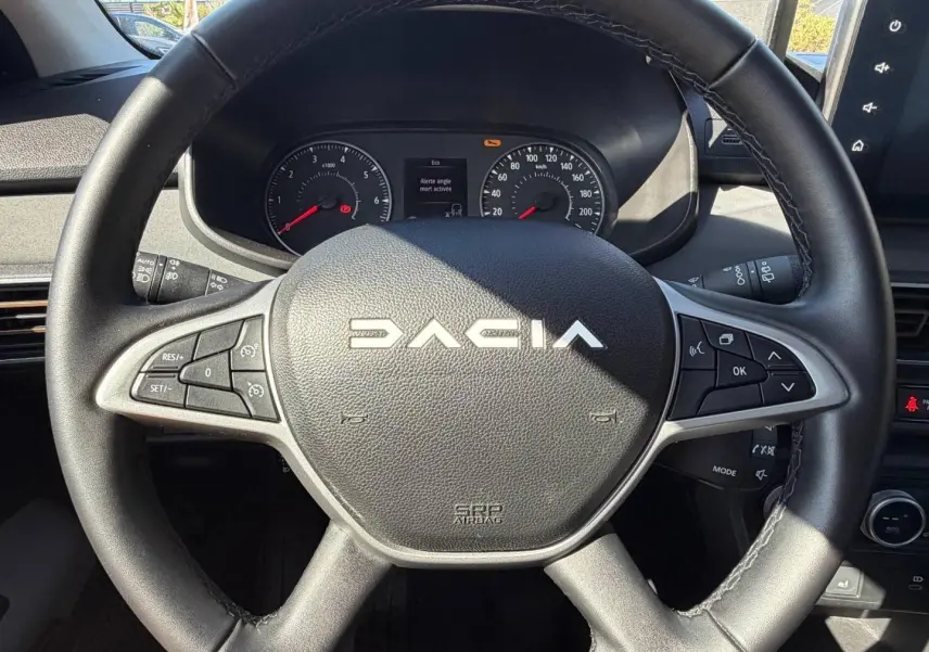 Vue rapprochée du volant noir de la Dacia Sandero 2025 avec commandes intégrées et tableau de bord visible.