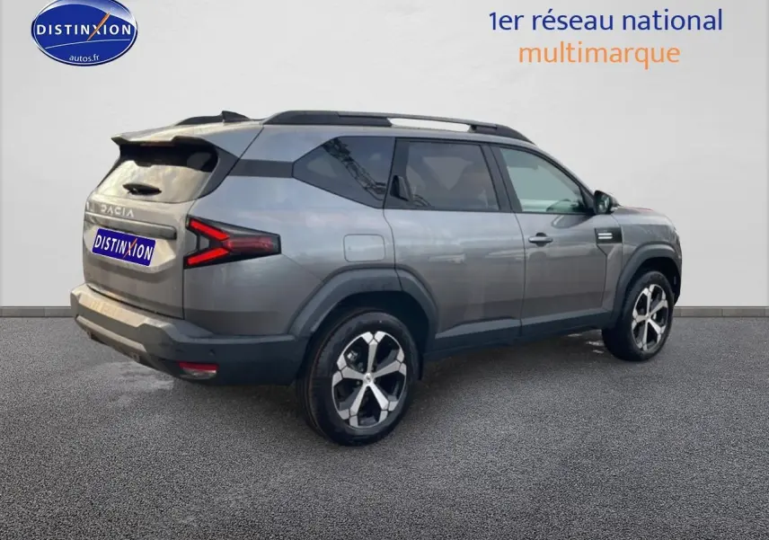 Vue 3/4 arrière droite du SUV Dacia Bigster gris schiste avec jantes alliage diamantées et barres de toit noires.