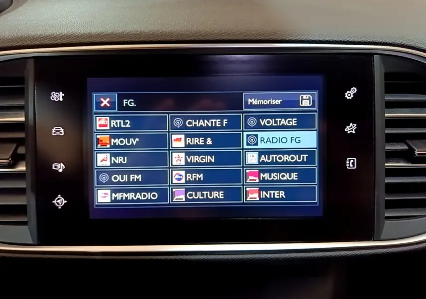 Écran tactile central affichant les stations radio dans l’habitacle d’une Peugeot 308 gris foncé, vue de face.
