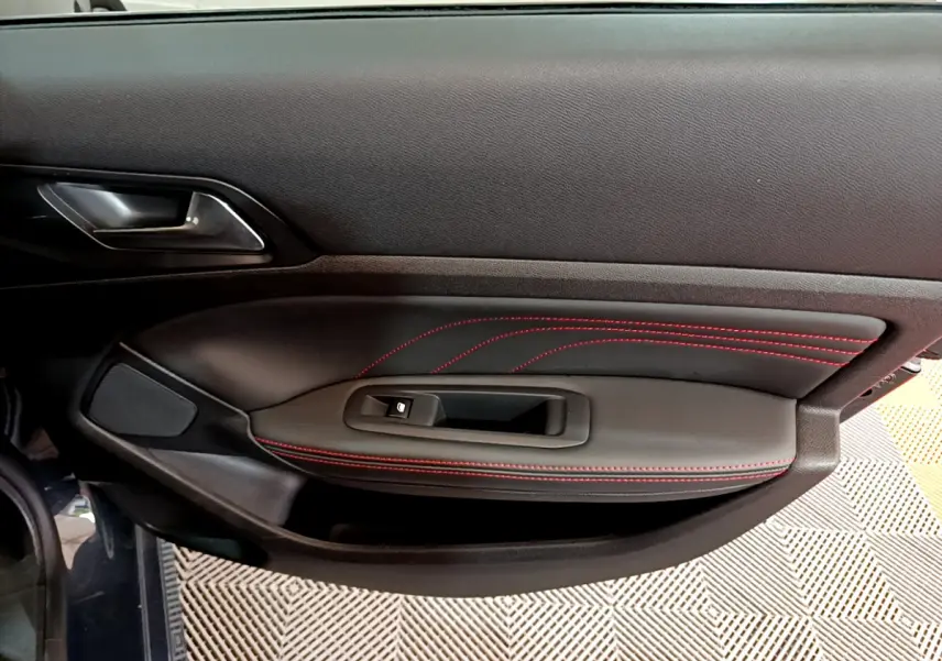Vue intérieure du panneau de porte côté gauche de la Peugeot 308 gris foncé avec surpiqûres rouges et commande de lève-vitre.
