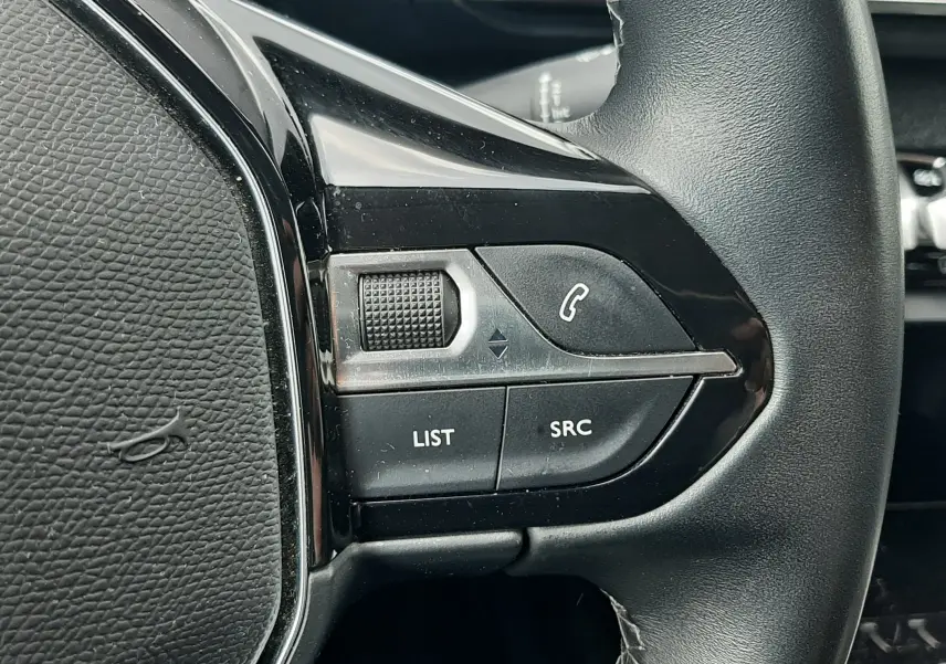 Gros plan sur les commandes gauche du volant noir en cuir du Peugeot 3008 gris Amazonite, boutons LIST et SRC visibles.