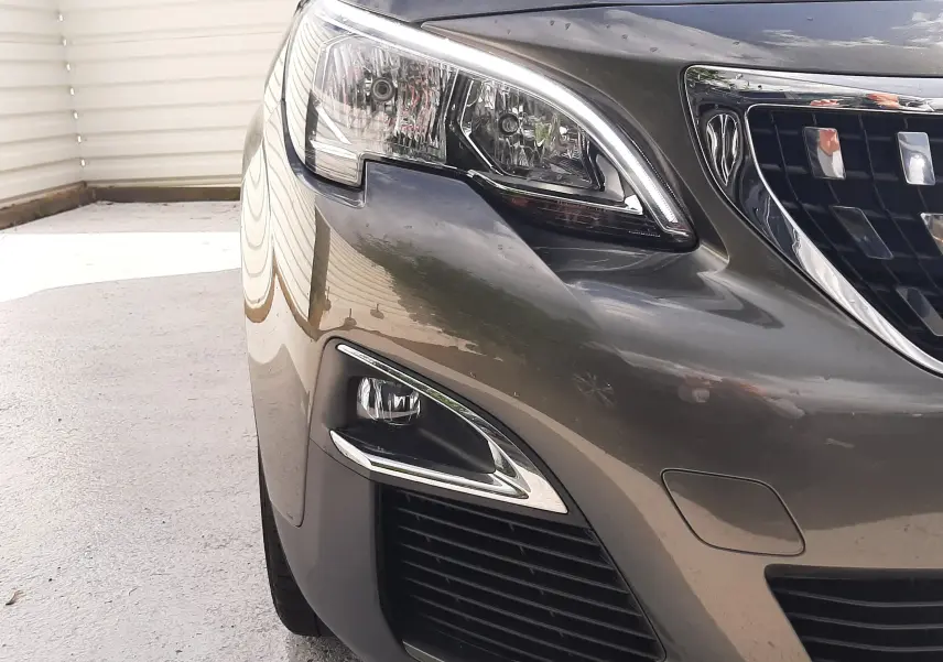 Gros plan sur l'avant droit du Peugeot 3008 gris amazonite, mettant en valeur le phare et la calandre chromée.