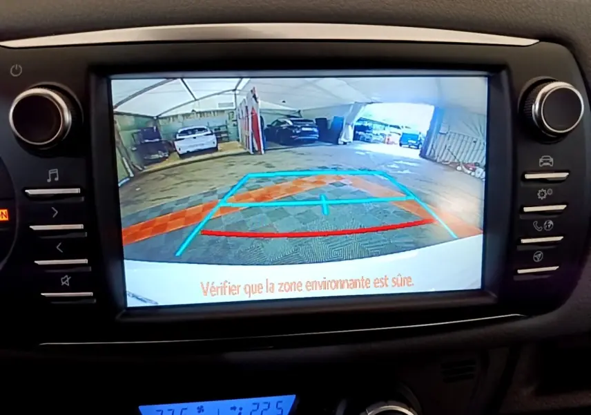 Écran tactile central montrant la caméra de recul d'une Toyota Yaris blanche dans un garage, avec repères de stationnement.