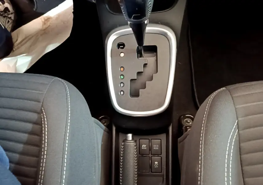Vue plongeante sur la console centrale de la Toyota Yaris hybride 2019, montrant la boîte auto et les sièges tissu gris.