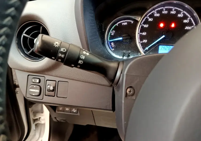 Vue rapprochée du tableau de bord côté gauche d'une Toyota Yaris blanche, avec commandes des phares et compteurs éclairés.