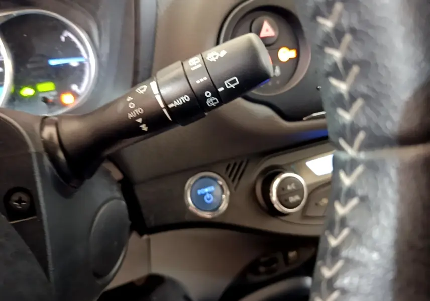 Gros plan intérieur sur le volant cuir et alu de la Toyota Yaris, avec commandes au volant et bouton start/stop bleu visible.