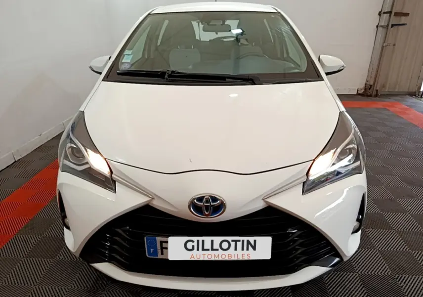 Vue avant d'une Toyota Yaris blanche de 2019 avec phares allumés et calandre noire distinctive.