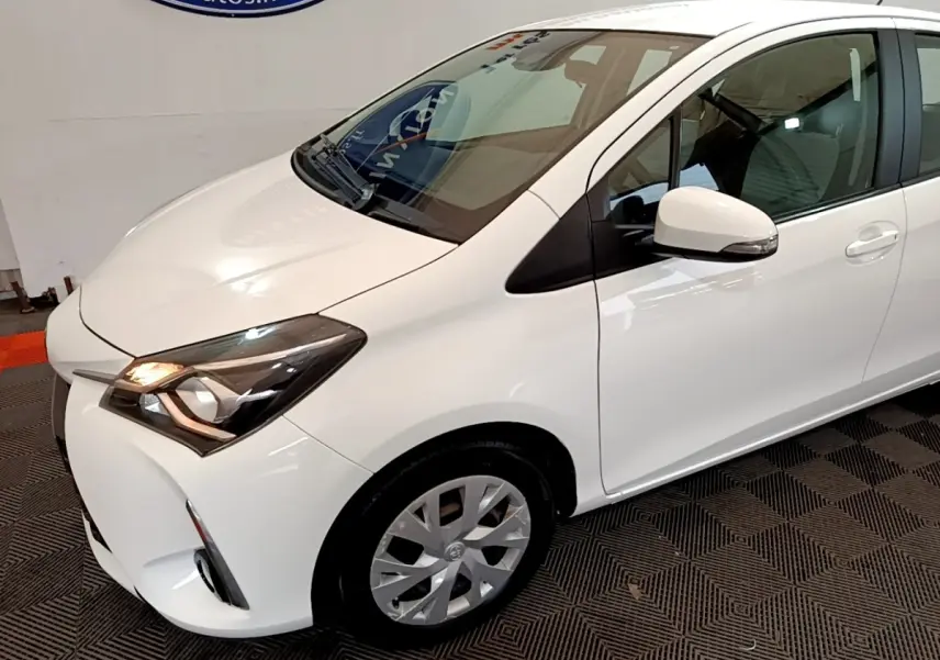 Vue 3/4 avant droit d'une Toyota Yaris blanche 2019 avec phares allumés et jantes alliage visibles.