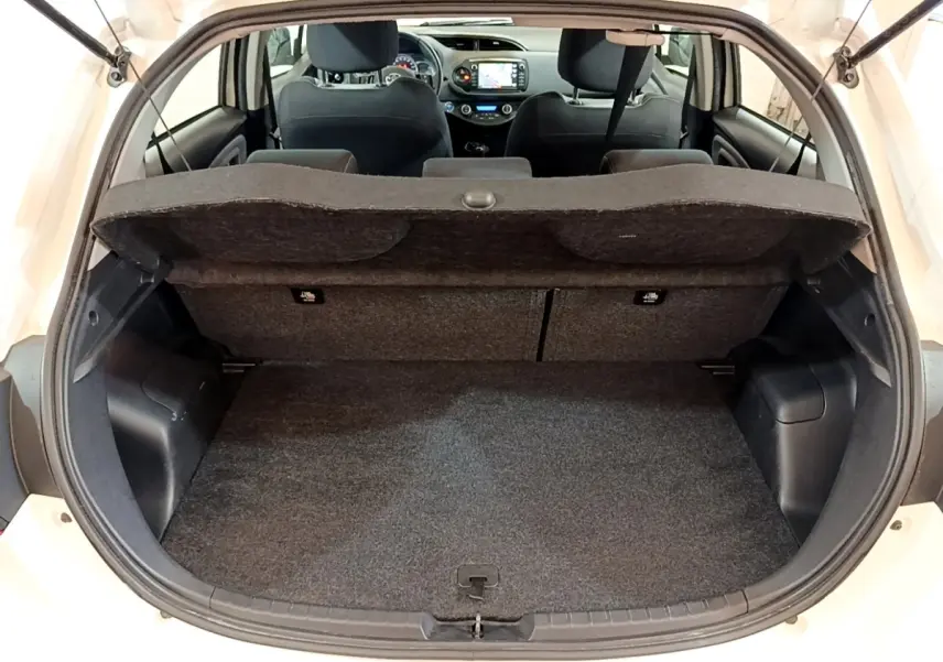 Vue arrière du coffre ouvert d'une Toyota Yaris blanche 2019, avec banquette arrière et tableau de bord visibles.