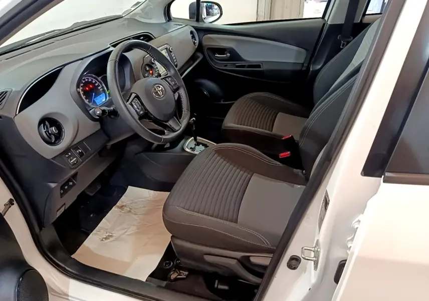 Vue intérieure côté conducteur de la Toyota Yaris blanche 2019, volant multifonctions en cuir et tableau de bord visible.