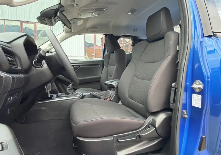 Vue intérieure côté conducteur du pick-up Isuzu D-MAX 2026 bleu Biarritz, sièges tissu et boîte manuelle visible.