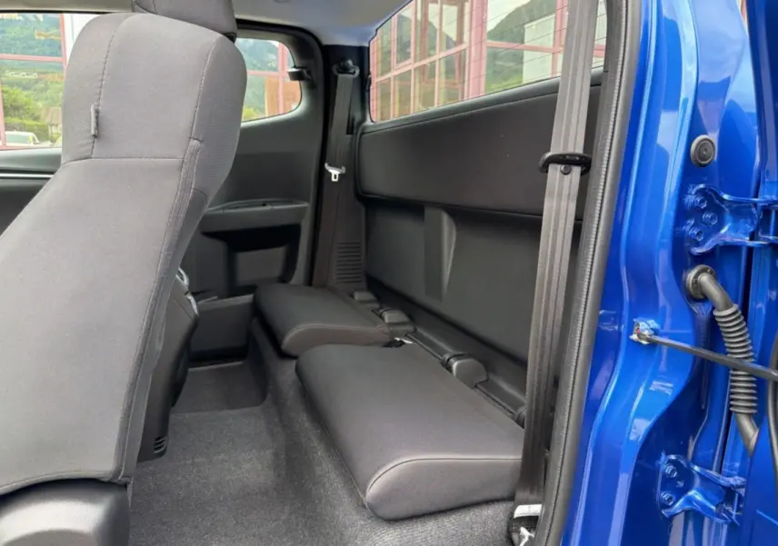 Vue intérieure côté arrière droit du pick-up Isuzu D-MAX bleu Biarritz, montrant les sièges arrière rabattus et la porte ouverte.