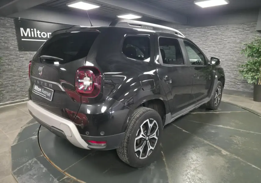 Vue 3/4 arrière droit du Dacia Duster noir nacré avec jantes alliage 17 pouces et barres de toit argentées.
