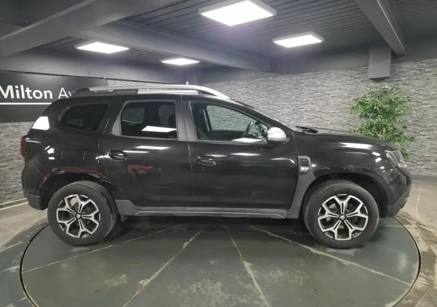 Vue de profil côté gauche d'un Dacia Duster noir nacré avec jantes alliage 17 pouces dans un showroom.